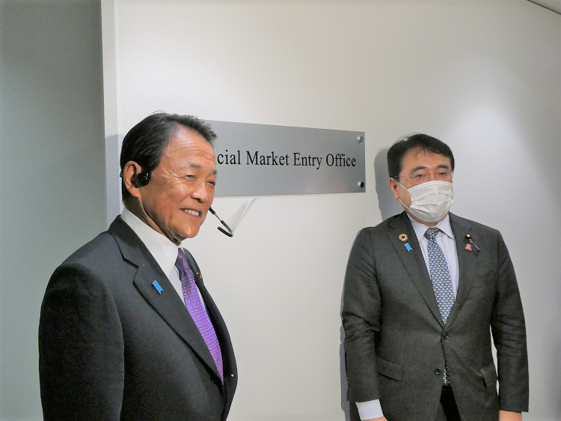 写真：設置した看板とともに報道陣の記念撮影に応じる 麻生大臣(左)と赤澤副大臣(右）